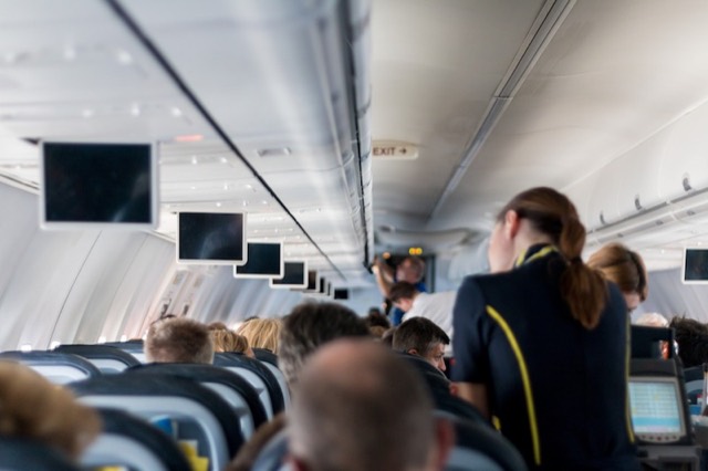 Vliegtuigcabine met passagiers en een stewardess in het gangpad